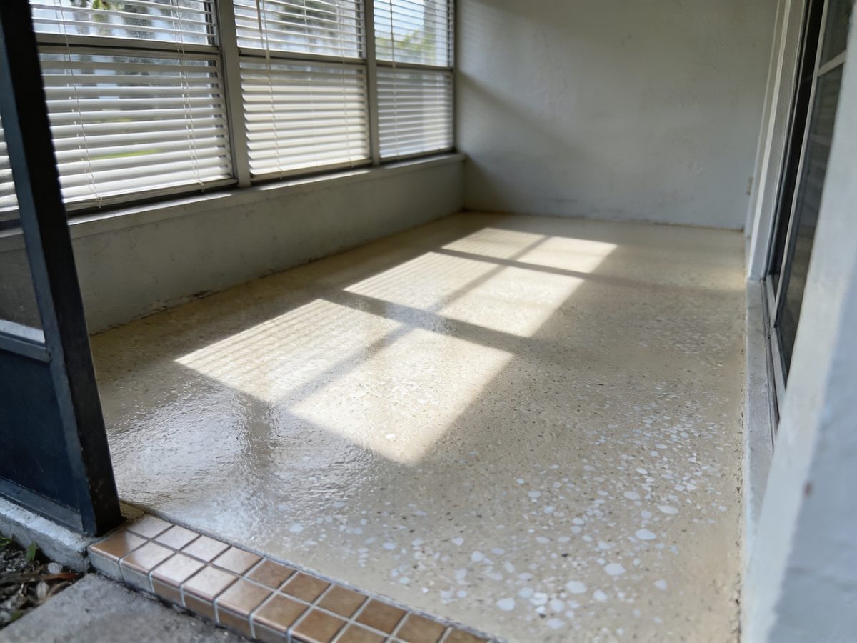 A ground-floor Florida room with a pale sand and white flake floor coating and jalousie windows throwing bands of daylight across it